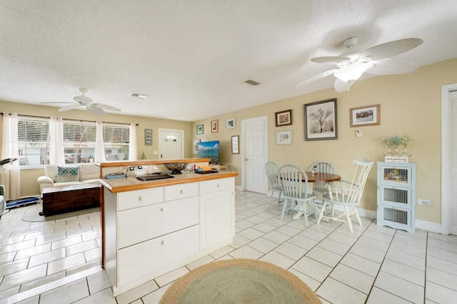 kitchen with white cabinetry, wood counters, a textured ceiling, and light tile patterned floors