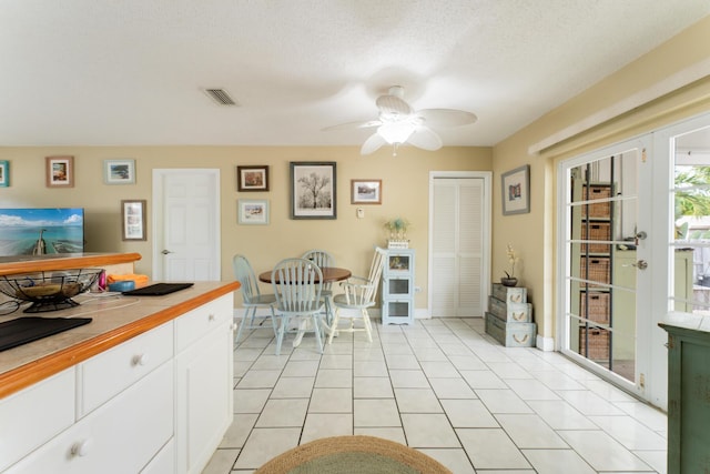 kitchen with light tile patterned flooring, a textured ceiling, white cabinets, and ceiling fan