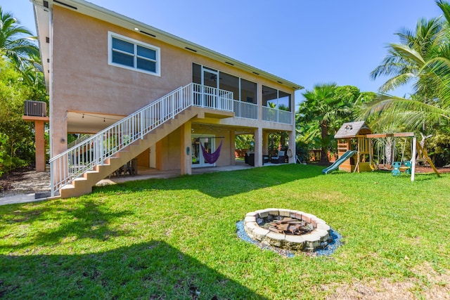 back of house featuring a patio area, an outdoor fire pit, a yard, a playground, and a sunroom