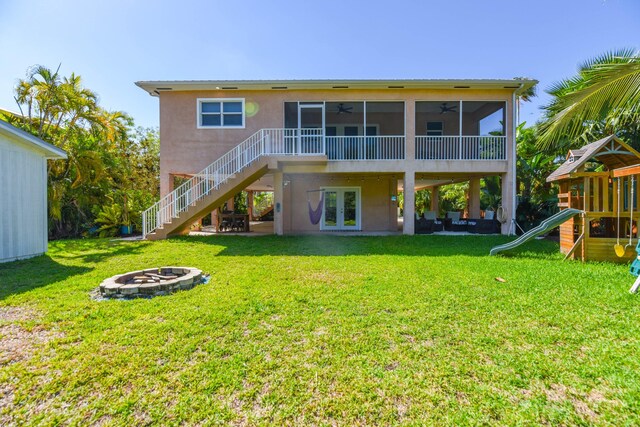 rear view of property with a lawn, an outdoor fire pit, ceiling fan, a playground, and a sunroom