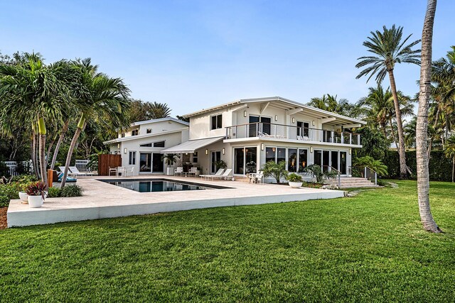 back of house with a balcony, a patio, and a lawn