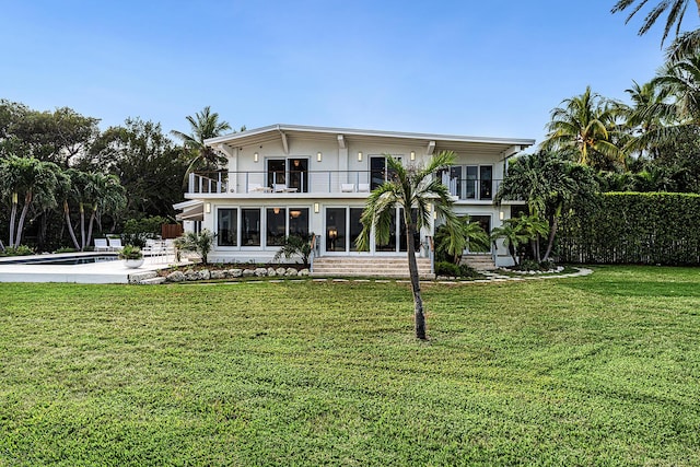 rear view of property with a balcony, a yard, a fenced in pool, and a sunroom