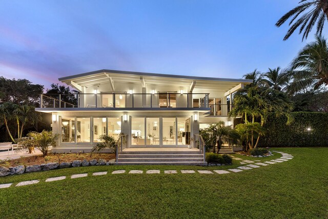 back house at dusk featuring a balcony and a lawn