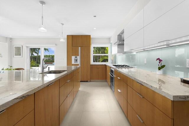 kitchen with decorative light fixtures, white cabinetry, sink, light stone countertops, and wall chimney exhaust hood