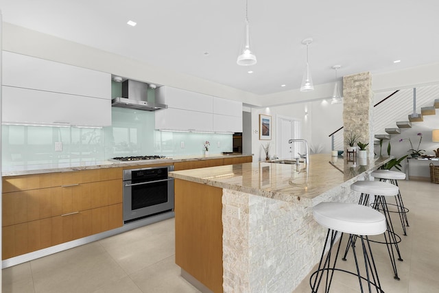 kitchen featuring sink, white cabinetry, hanging light fixtures, stainless steel oven, and wall chimney exhaust hood