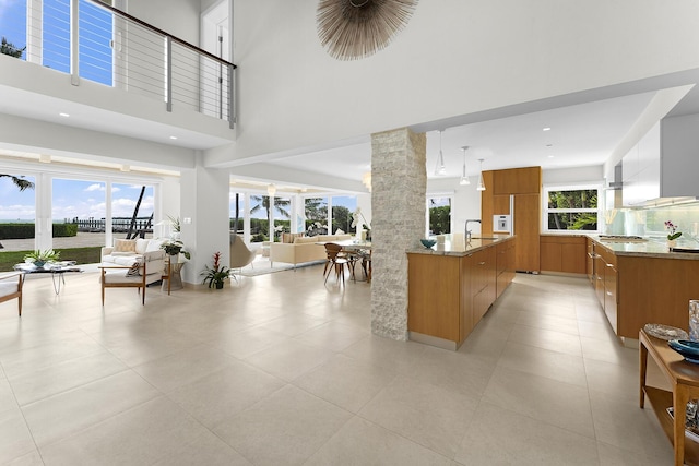 kitchen with stainless steel gas cooktop, ornate columns, light stone counters, decorative light fixtures, and a towering ceiling