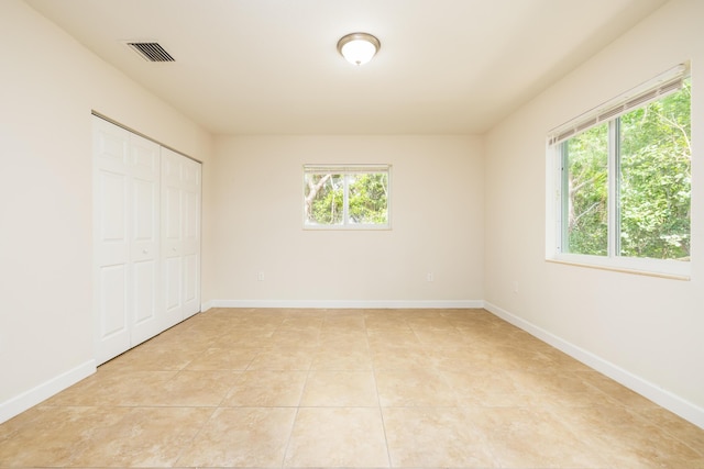 unfurnished bedroom with multiple windows, light tile patterned floors, and a closet