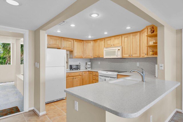 kitchen featuring light brown cabinetry, sink, white appliances, and kitchen peninsula