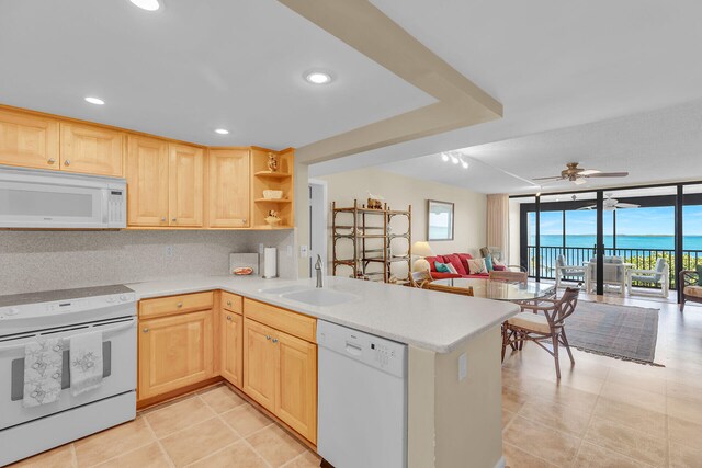 kitchen featuring sink, white appliances, expansive windows, light brown cabinetry, and kitchen peninsula