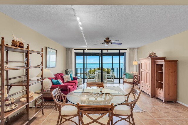 tiled dining room with floor to ceiling windows, a water view, ceiling fan, and a textured ceiling