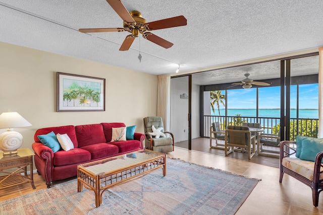 living room with ceiling fan, floor to ceiling windows, a textured ceiling, and a water view