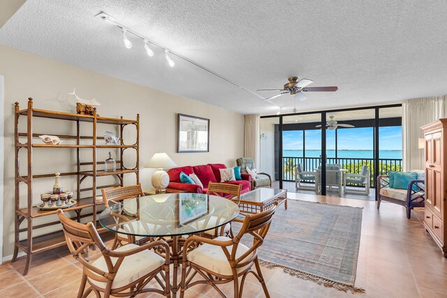 tiled living room with ceiling fan, floor to ceiling windows, a water view, track lighting, and a textured ceiling