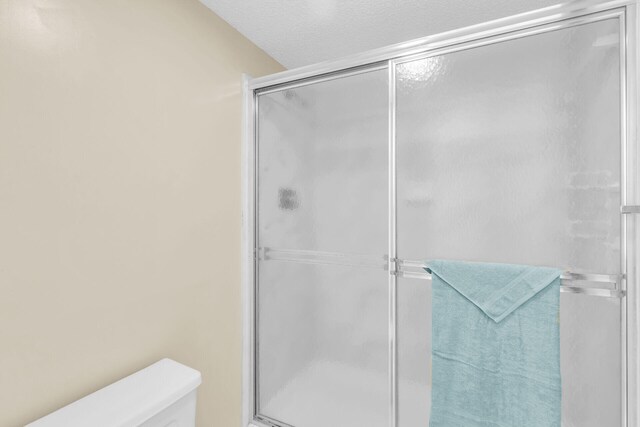 bathroom with an enclosed shower, a textured ceiling, and toilet