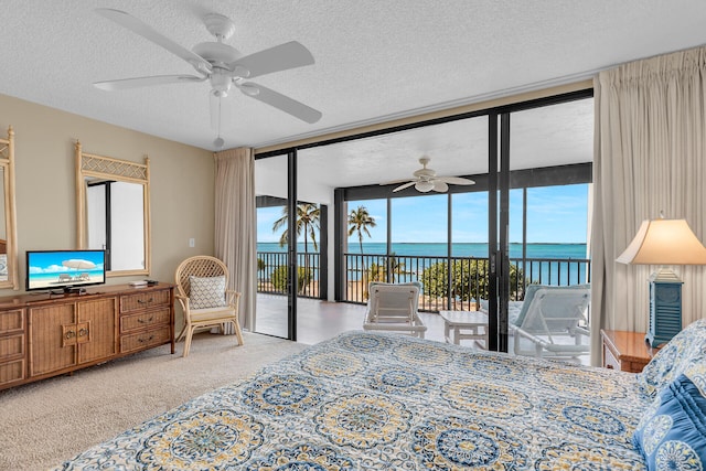 bedroom with floor to ceiling windows, a water view, a textured ceiling, carpet floors, and access to exterior