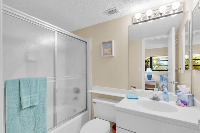 full bathroom with shower / bath combination with glass door, vanity, toilet, and a textured ceiling