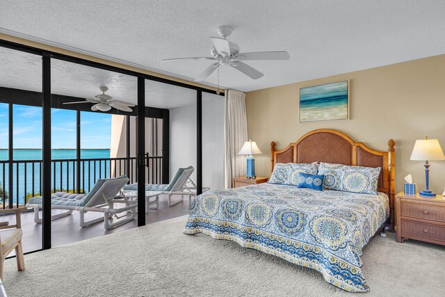 carpeted bedroom with a water view, a textured ceiling, expansive windows, ceiling fan, and access to exterior