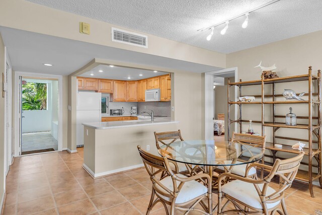 dining space featuring sink, light tile patterned floors, track lighting, and a textured ceiling