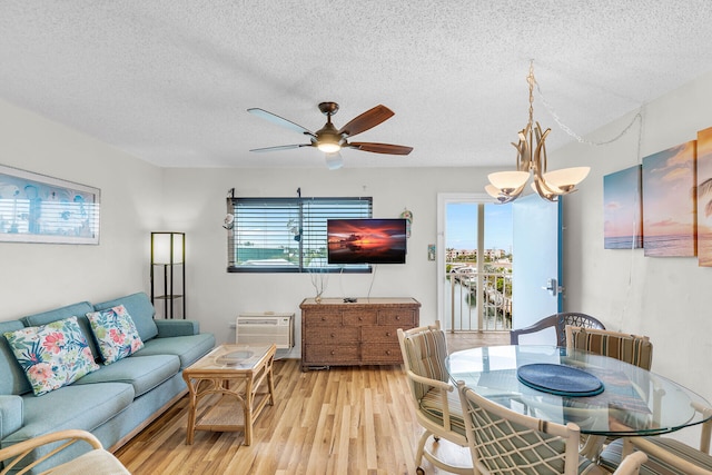 living room with a wall mounted air conditioner, ceiling fan with notable chandelier, light hardwood / wood-style floors, and a textured ceiling