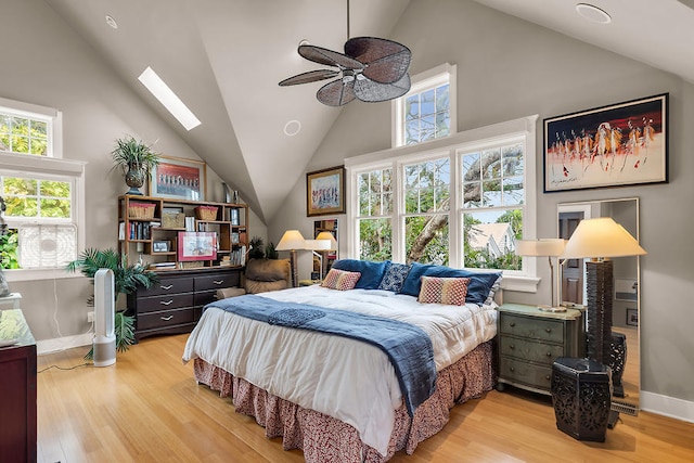 bedroom with multiple windows, high vaulted ceiling, a skylight, and light hardwood / wood-style floors