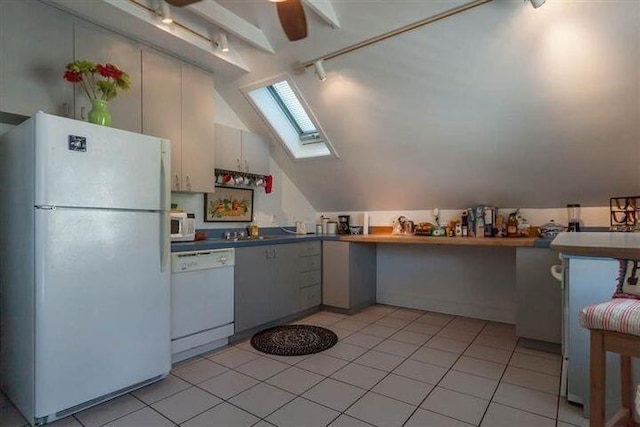 kitchen featuring light tile patterned flooring, white appliances, and vaulted ceiling with skylight