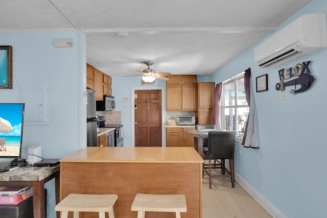 kitchen featuring a wall mounted AC, appliances with stainless steel finishes, a kitchen breakfast bar, ceiling fan, and decorative backsplash