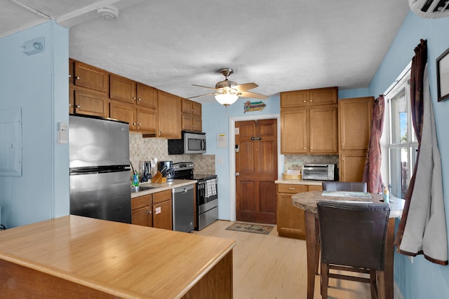 kitchen featuring light hardwood / wood-style flooring, ceiling fan, stainless steel appliances, a wall unit AC, and decorative backsplash