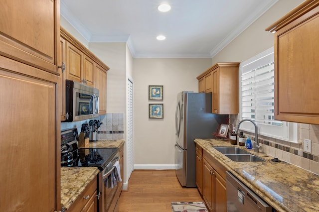 kitchen featuring a sink, baseboards, ornamental molding, appliances with stainless steel finishes, and light wood finished floors