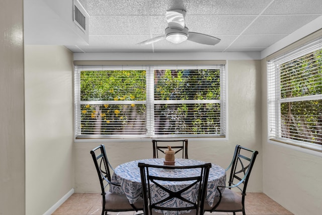 tiled dining space with ceiling fan and a drop ceiling