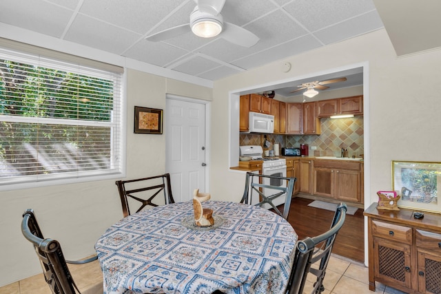 dining room with sink, a paneled ceiling, ceiling fan, and light tile patterned flooring