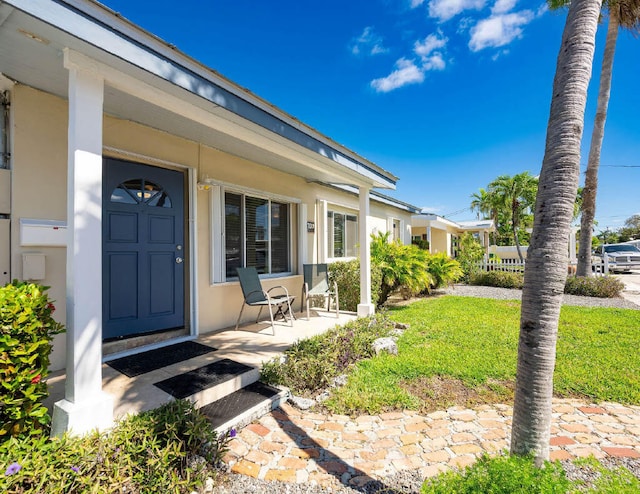 entrance to property with a yard, a porch, and stucco siding