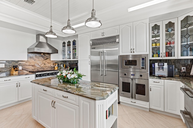 kitchen with white cabinetry, wall chimney range hood, built in appliances, and dark stone counters