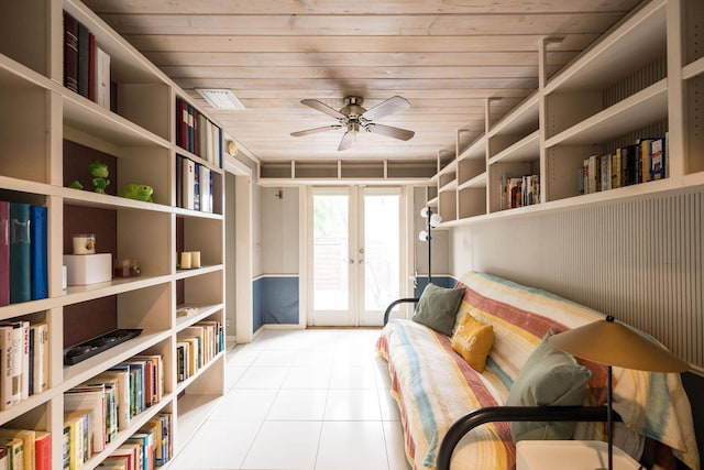 living area with wall of books, light tile patterned flooring, a ceiling fan, and french doors