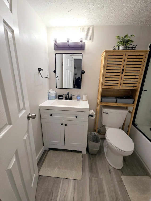 full bath with visible vents, toilet, a textured ceiling, vanity, and wood finished floors