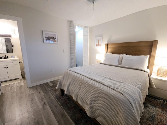 bedroom with a sink, connected bathroom, baseboards, and wood finished floors