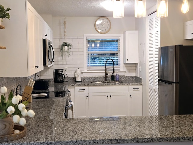 kitchen featuring appliances with stainless steel finishes, white cabinetry, a sink, and decorative light fixtures