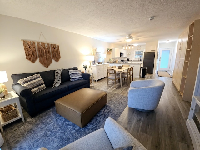 living area with ceiling fan, a textured ceiling, and wood finished floors