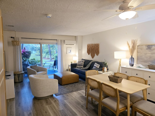 living area with visible vents, a ceiling fan, a wall unit AC, wood finished floors, and a textured ceiling