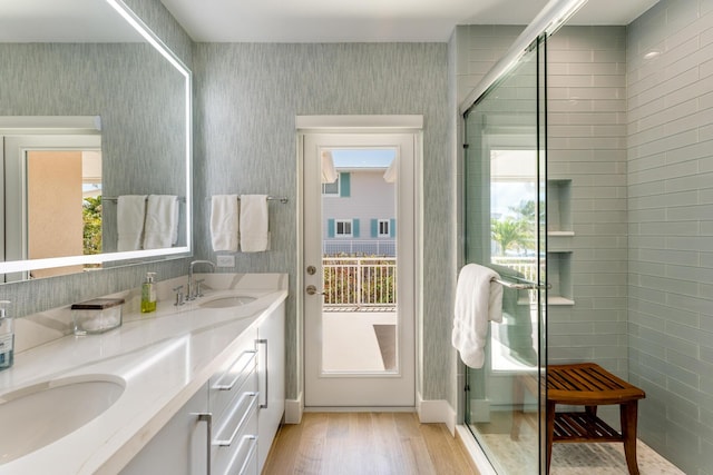 bathroom with wood finished floors, a shower stall, wallpapered walls, and double vanity