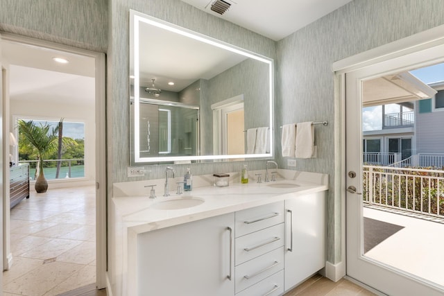 bathroom with wallpapered walls, double vanity, and a shower