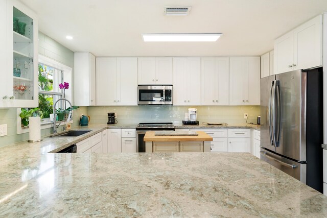 19 N Dr, Key Largo, FL 33037 - kitchen featuring appliances with stainless steel finishes, decorative backsplash, glass insert cabinets, light stone counters, and white cabinets