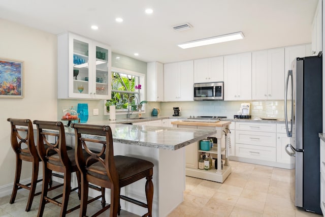 19 N Dr, Key Largo, FL 33037 - kitchen featuring appliances with stainless steel finishes, a peninsula, light stone countertops, a breakfast bar, and decorative backsplash