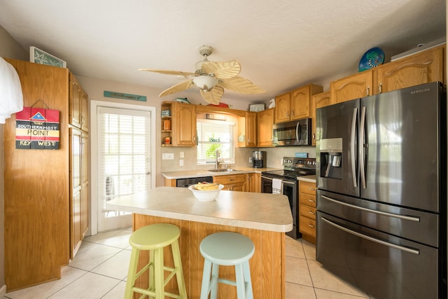 kitchen with appliances with stainless steel finishes, sink, a kitchen bar, a center island, and light tile patterned floors