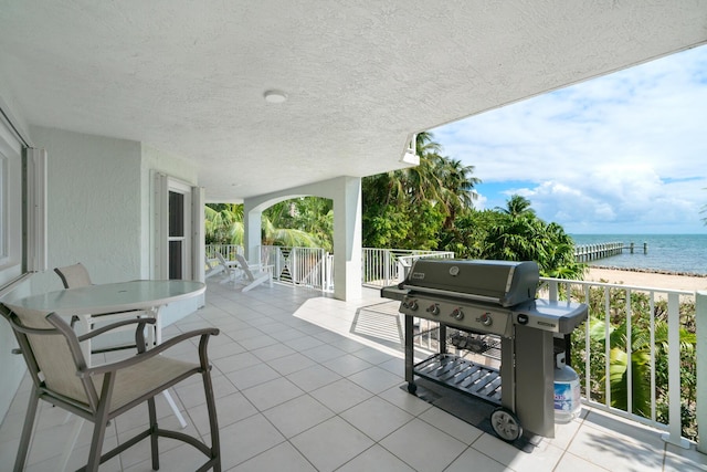 view of patio / terrace featuring a water view, a balcony, a grill, and a view of the beach