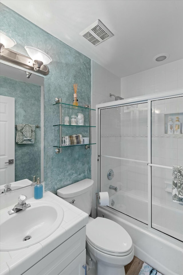 bathroom with toilet, bath / shower combo with glass door, wood finished floors, vanity, and visible vents