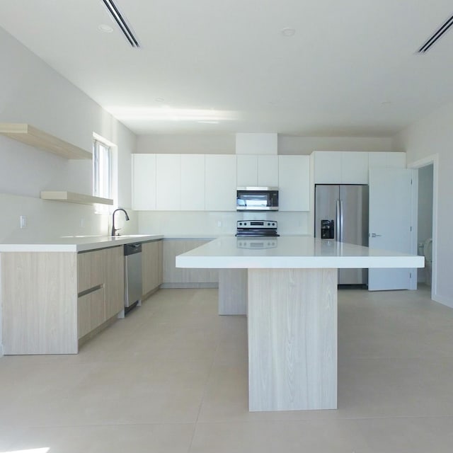 kitchen featuring light tile patterned flooring, sink, white cabinetry, appliances with stainless steel finishes, and a kitchen island