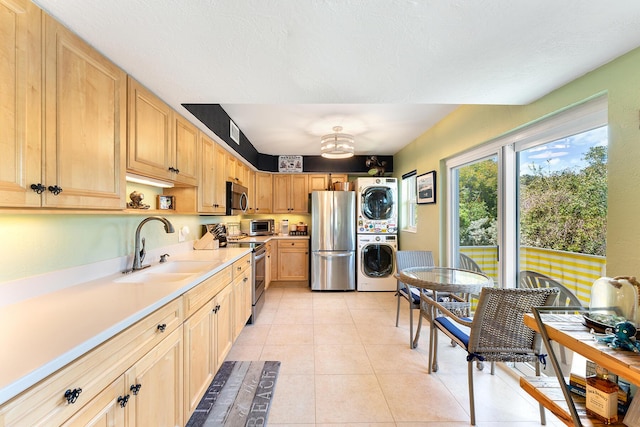 kitchen with light tile patterned floors, sink, appliances with stainless steel finishes, stacked washer / drying machine, and light brown cabinetry