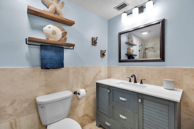 bathroom featuring visible vents, toilet, vanity, a textured ceiling, and tile walls