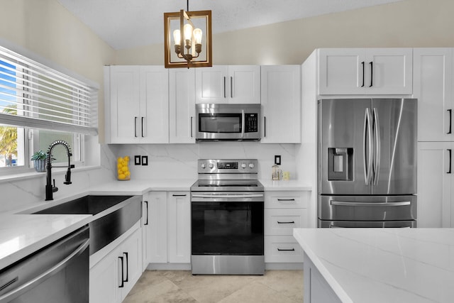 kitchen with a sink, decorative backsplash, stainless steel appliances, white cabinets, and a notable chandelier