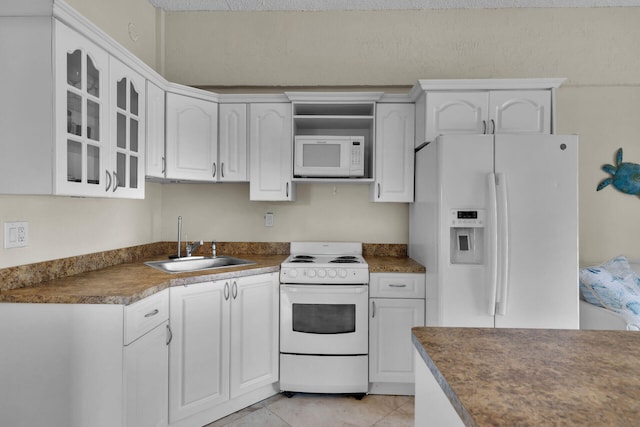 kitchen featuring a sink, dark countertops, white cabinetry, white appliances, and glass insert cabinets