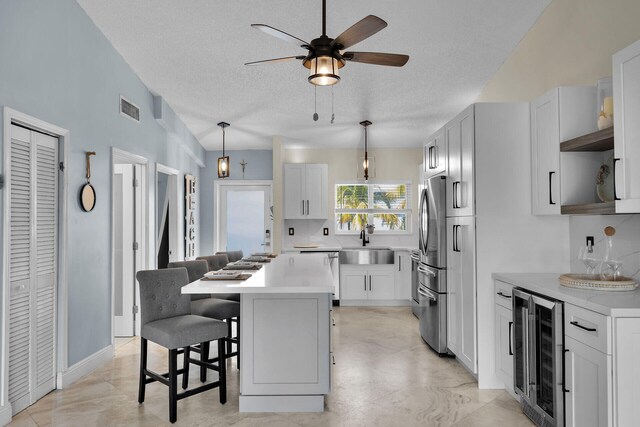 kitchen with beverage cooler, visible vents, freestanding refrigerator, a sink, and a kitchen breakfast bar